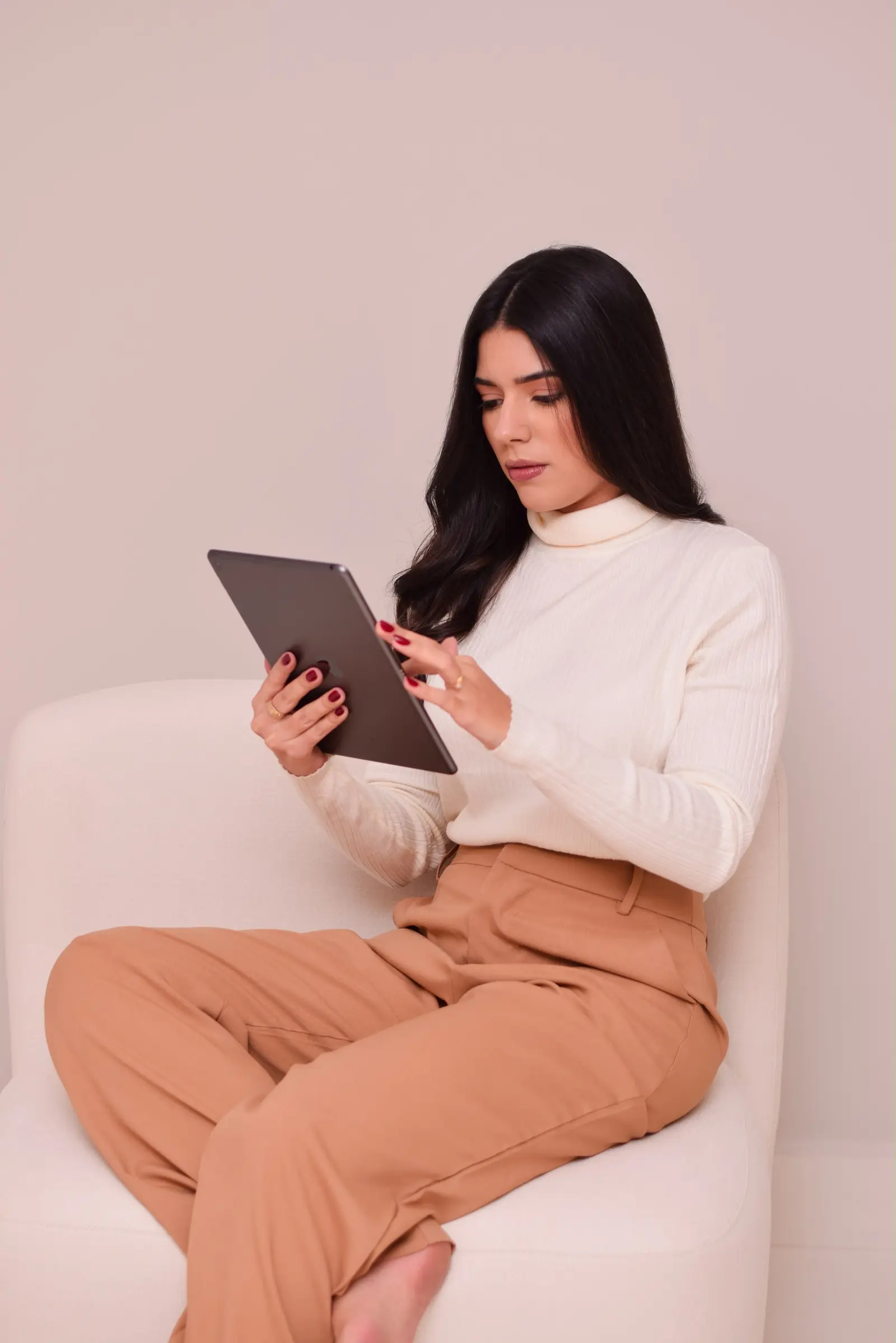 Júlia sentada numa poltrona clara, trabalhando num tablet