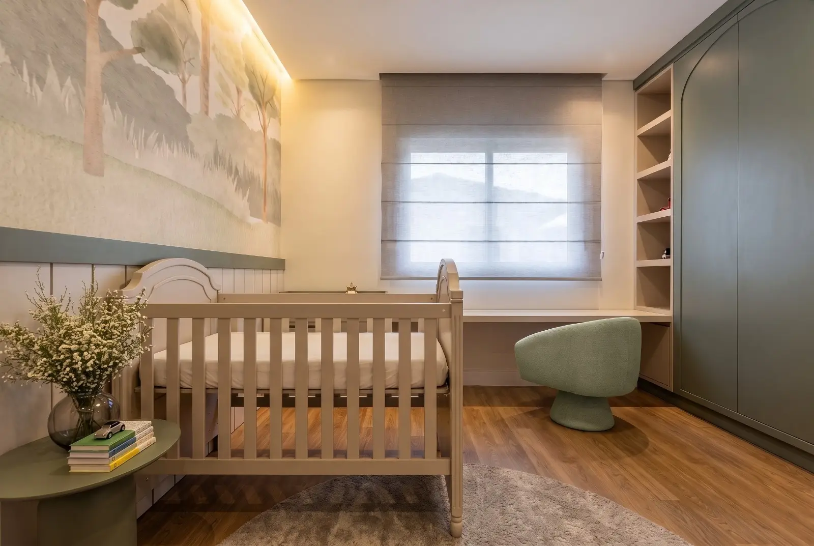Quarto de bebê com mural de floresta em aquarela, berço claro e poltrona verde